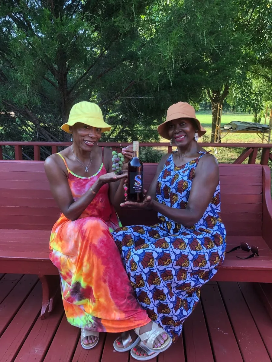 Two women holding grapes and a wine bottle at Young Family Farm